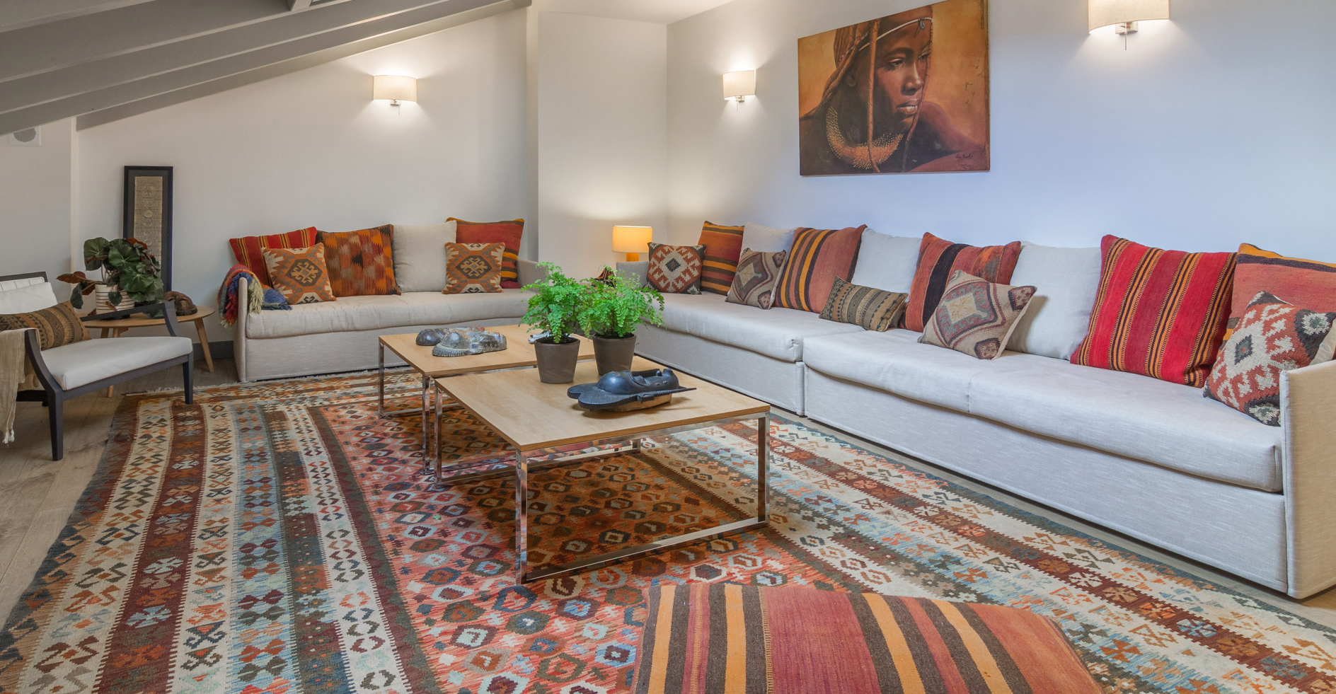 Vivienda diseñada por Tribeca. Sala de estar decorada con alfombra y cojines kilim, máscaras africanas y cuadro representando a un guerrero masai.   